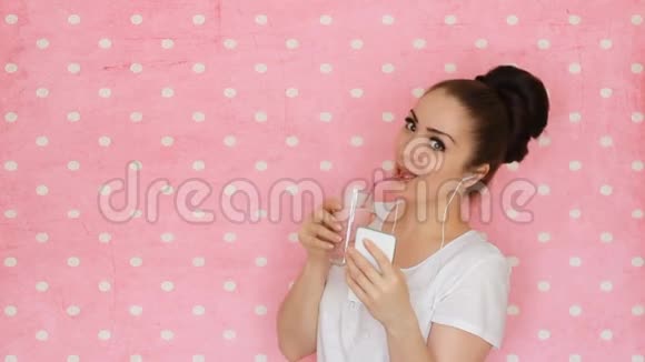 年轻的女人用她的智能手机用粉色背景的吸管喝冰沙视频的预览图