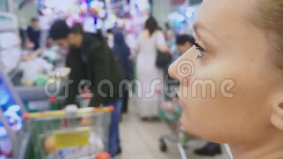 一个年轻无聊的女人在超市里路过的顾客的画像4k模糊视频的预览图