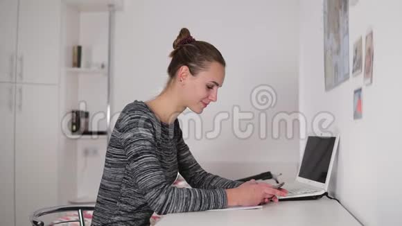 漂亮的女人坐在桌子旁在办公室里用手机发短信和上网视频的预览图