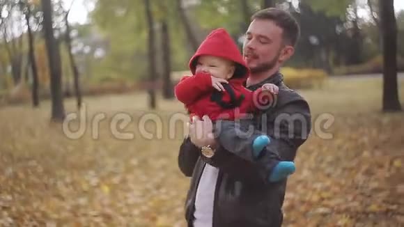 一位年轻的父亲正和一个婴儿在一个阳光明媚的秋日玩耍在城市公园里开心地笑着视频的预览图