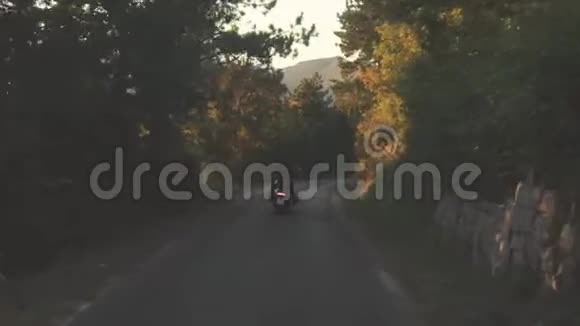 从后面的人骑摩托车在森林道路上库存乘坐黑色皮夹克的摩托车手的后景视频的预览图