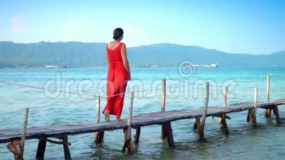 穿着红色长裙走在码头上的美女PhuQuoc岛慢吞吞的旅行者走在码头上视频的预览图