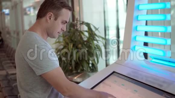 在机场航站楼穿灰色T恤的帅哥用触摸屏搜索他的航班信息视频的预览图