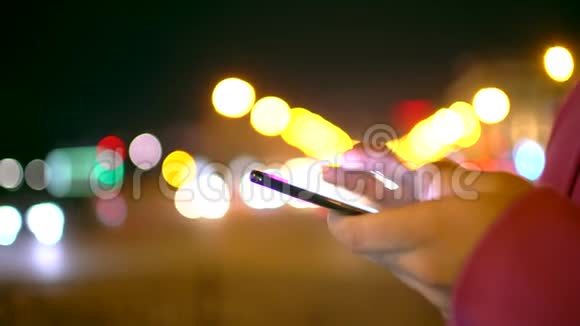 一个年轻人正在上下班晚上在繁忙的城市街道上浏览他的手机视频的预览图