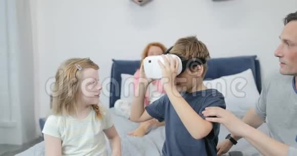 哥哥给妹妹戴上虚拟现实眼镜和父母一起在卧室里度过早晨家庭娱乐视频的预览图
