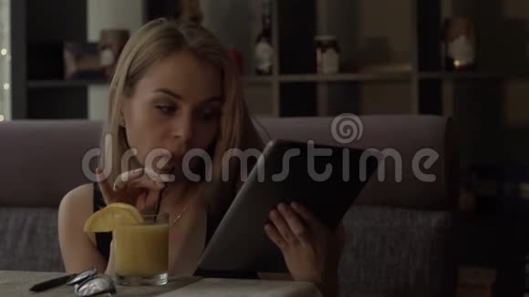 美丽的女人从玻璃上喝橙汁在平板电脑上打字视频的预览图
