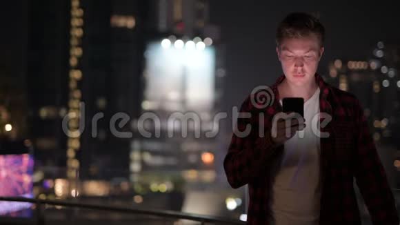 年轻的帅哥晚上用电话来看城市视频的预览图