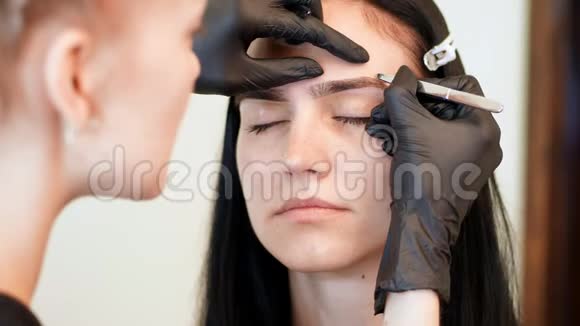 美容院特写戴黑色橡胶手套的化妆师的手拿着镊子拔出眉毛硕士视频的预览图