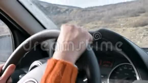 一只穿着橙色毛衣的雌性手在城外开着一辆车慢动作妇女开车视频的预览图