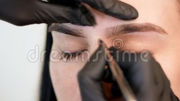 美容院特写戴黑色橡胶手套的化妆师的手拿着镊子拔出眉毛硕士视频的预览图