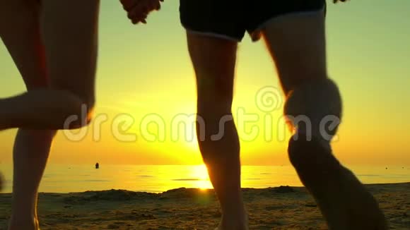快乐的一对夫妇沿着海滩奔跑手牵着夕阳背景慢动作一对夫妇的剪影视频的预览图