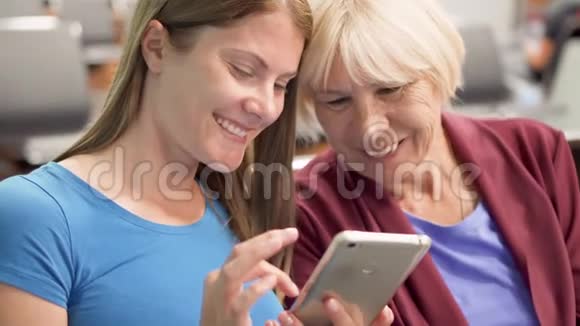 年长的母亲和她的小女儿坐在机场候机楼等待使用智能手机的航班视频的预览图