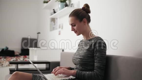 坐在沙发上的年轻女人一边看一边用手提电脑打字快速看屏幕视频的预览图