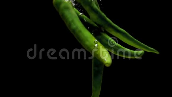 绿色辣椒在黑色背景下落入透明水视频的预览图