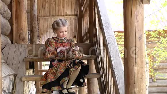 穿着传统服装的小漂亮女孩坐在一座古老的乡村木屋前台阶上的肖像全额视频的预览图