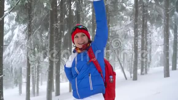 有趣的旅游女孩向某人挥手走在山上一片白雪覆盖的针叶林上视频的预览图