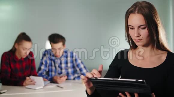 年轻的集中精力的女商人站在办公室里一边用她的平板电脑而她的同事们正在做这项工作视频的预览图