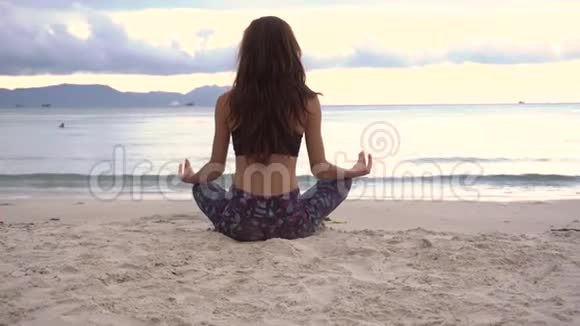 在海滩上坐莲花座的年轻女子视频的预览图