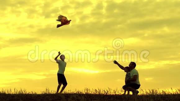 快乐的家庭父亲和孩子们在草地上奔跑夏天在日落时带着风筝缓慢地运动家庭户外视频的预览图