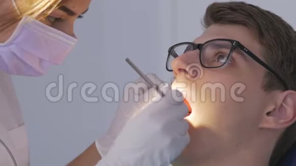一位女牙医检查坐在椅子上的年轻人的口腔视频的预览图
