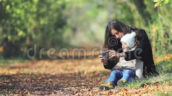妈妈带宝宝户外用手机秋叶背景视频的预览图