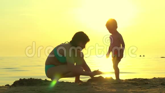 海滩上的幸福家庭妈妈和孩子在海上日落的背景下建造一座沙堡a的概念视频的预览图