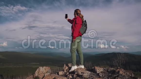 一位女游客正在山区的社交网络上直播或在智能手机上录制视频视频的预览图
