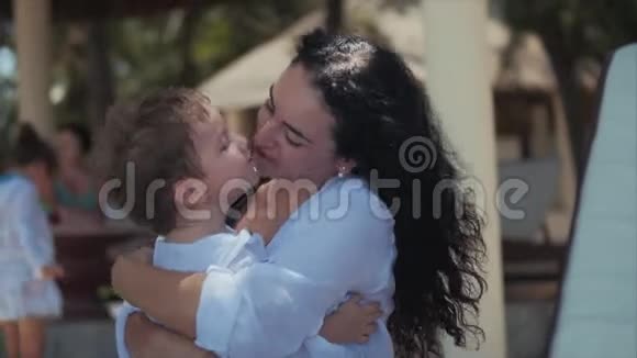 快乐的母亲在海岸拥抱她的孩子可爱的孩子亲吻他的妈妈轻轻拥抱儿童户外运动概念妈妈视频的预览图