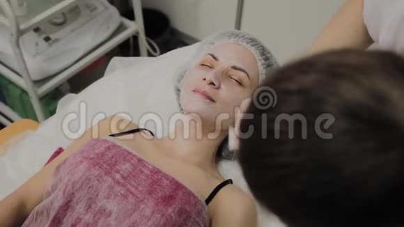熟练的美容师在室内水疗沙龙里给躺着的女人戴上面具视频的预览图