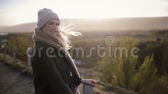 年轻美丽的女人站在桥上在寒冷的晴天享受风景头发迎风飘扬视频的预览图