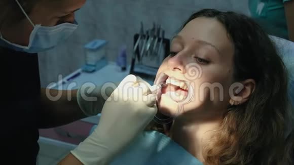牙医在安装托架系统之前将牙齿上的正畸胶水涂在门闩上的妇女身上访问视频的预览图