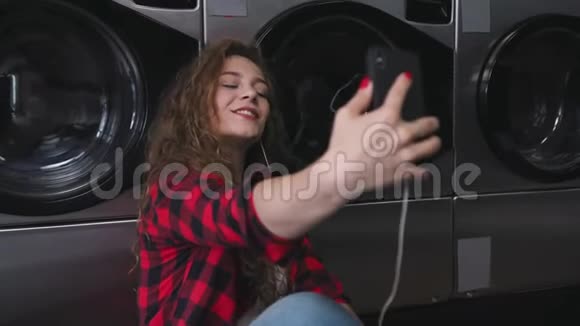 年轻漂亮的女人红色的卷发穿着红色的酒石衬衫听音乐打电话洗衣店跳舞视频的预览图