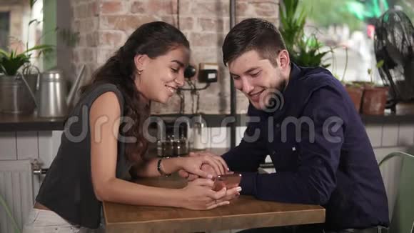 浪漫的年轻夫妇牵着手在咖啡店里用电话娱乐浪漫的约会视频的预览图