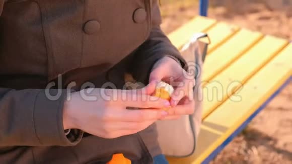 年轻的黑发女人戴着太阳镜剥着橘子坐在公园的长凳上特写双手视频的预览图