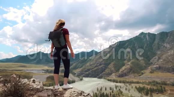 一个背着背包的旅行者站在山崖边举起双手背面视图视频的预览图