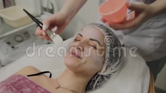 熟练的美容师在室内水疗沙龙里给躺着的女人戴上面具视频的预览图