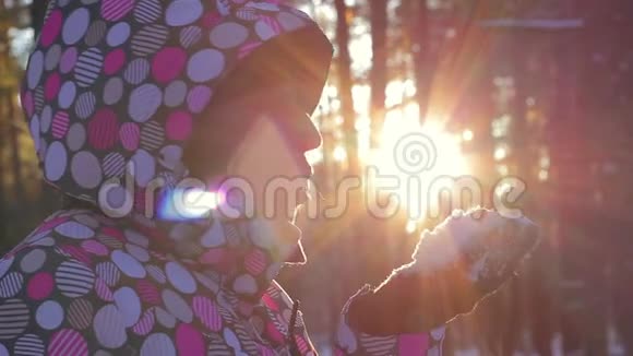 快乐的女人从手中吹雪花在日落时微笑有眩光的效果冬天的森林和日落的女人视频的预览图