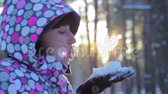 女人从手中吹起雪花在日落时微笑有眩光的效果冬天的森林和日落的女人视频的预览图