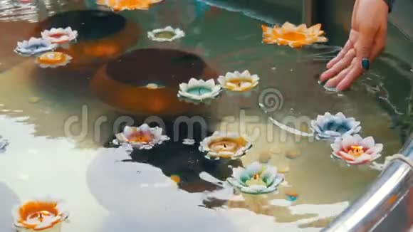 女人手把一支燃烧的蜡烛滴在池塘里的莲花形状上视频的预览图