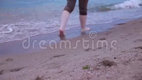 在日落时分赤脚沿着沙滩上的海浪走近沿着海滩和海浪散步的女人的腿视频的预览图