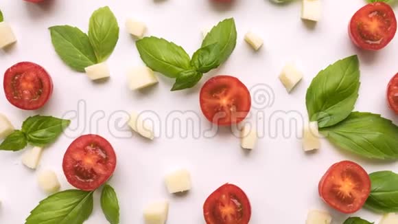 樱桃西红柿奶酪和新鲜的绿色罗勒叶白色背景特写镜头在顶部移动视频的预览图