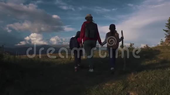 旅行者穿过群山一个年轻的女人和两个孩子去野营带背包的游客背面视图视频的预览图
