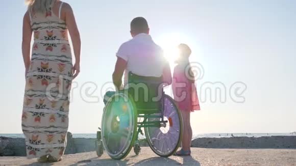 配偶在轮椅上拥抱妻子和背光的小女孩家人互相拥抱残疾男子与妻子和女儿视频的预览图