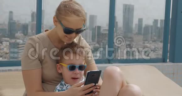 在以色列特拉维夫的酒店屋顶放松时妈妈和孩子使用手机视频的预览图