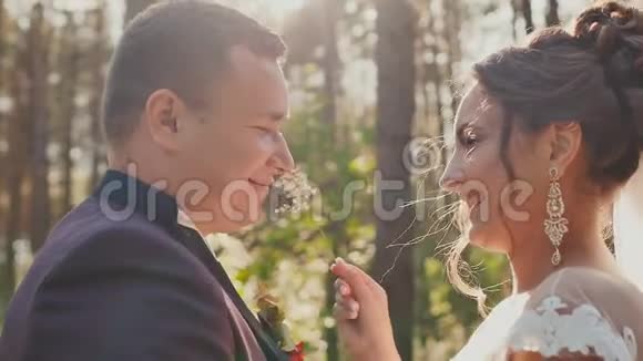 新娘和新郎相爱在阳光下美丽的绿色森林里互相看着新婚夫妇的近脸视频的预览图