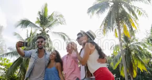 个人团体在棕榈树下的手机户外自助拍照快乐的微笑混合种族男人和女人视频的预览图