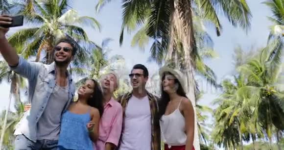 个人团体在棕榈树下的手机户外自助拍照快乐的微笑混合种族男人和女人视频的预览图