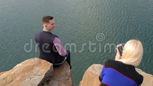 女孩在海边的悬崖边拍男人的照片视频的预览图