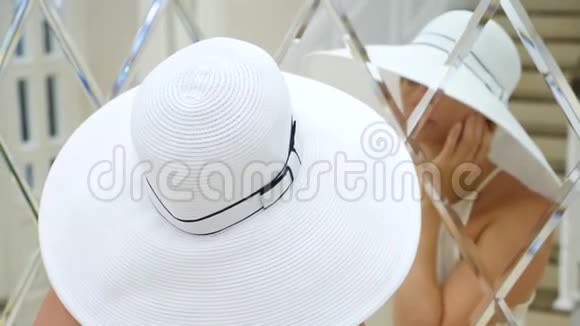 一个戴着白色大帽子和白色连衣裙的女人看着镜子4k慢动作视频的预览图