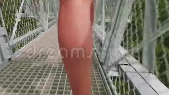 镜头跟随着白种人女子穿着运动鞋在高高的高山上的悬索桥上行走视频的预览图